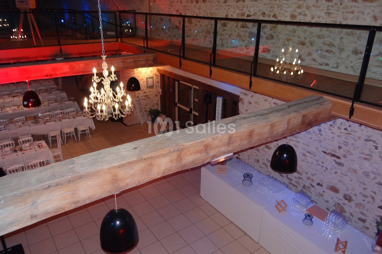 Salle de réception avec tables dressées, lustres suspendus et mezzanine en bois et verre.