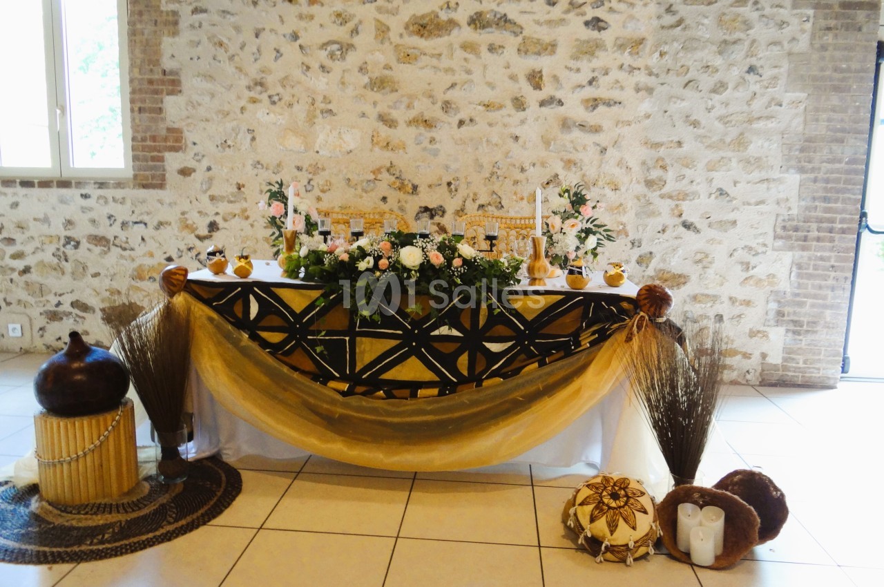 Table décorée avec des fleurs, bougies et tissus dorés, dans une salle en pierre avec lumière naturelle.
