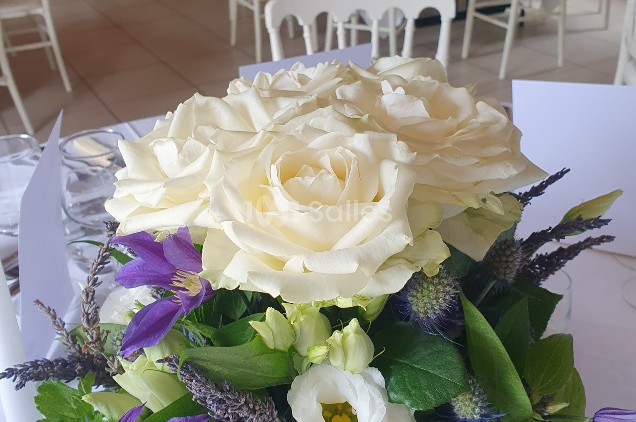 Bouquet de fleurs comprenant des roses blanches, des lavandes et des feuillages, posé sur une table dressée.