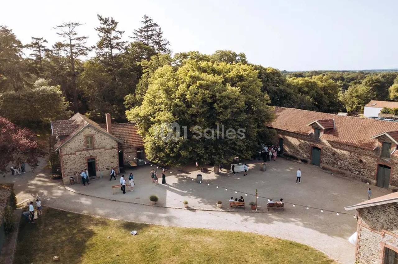 Vue aérienne d'une cour entourée de bâtiments en pierre, avec des arbres et des personnes rassemblées en petits groupes.