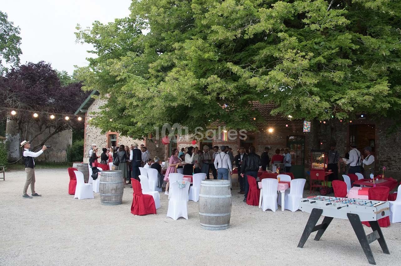 Groupe de personnes rassemblées dans une cour extérieure décorée, avec tables, chaises et guirlandes lumineuses.
