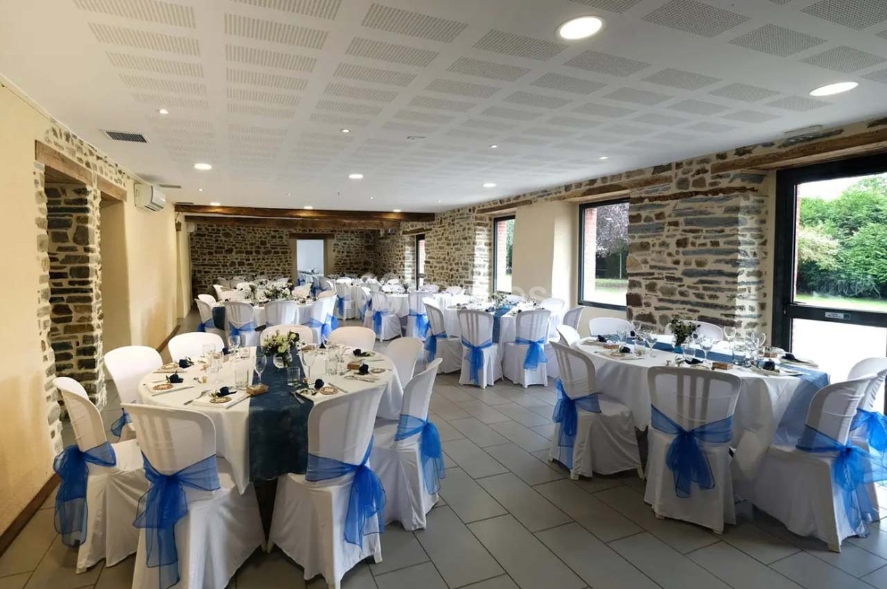 Salle de réception décorée avec des tables rondes, nappes blanches et nœuds bleus sur les chaises.