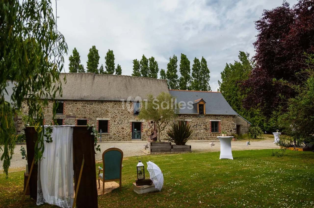 Bâtiment en pierre avec toit en ardoise, entouré d'arbres, pelouse aménagée avec mobilier et décorations.