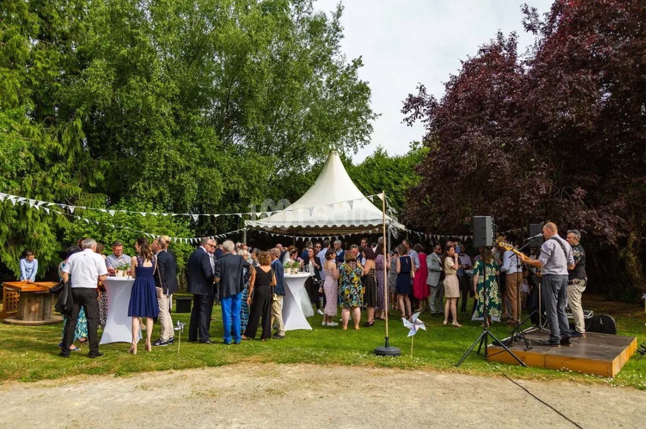 Groupe de personnes rassemblées dans un jardin autour de tables sous une tente blanche lors d'un événement en plein air.