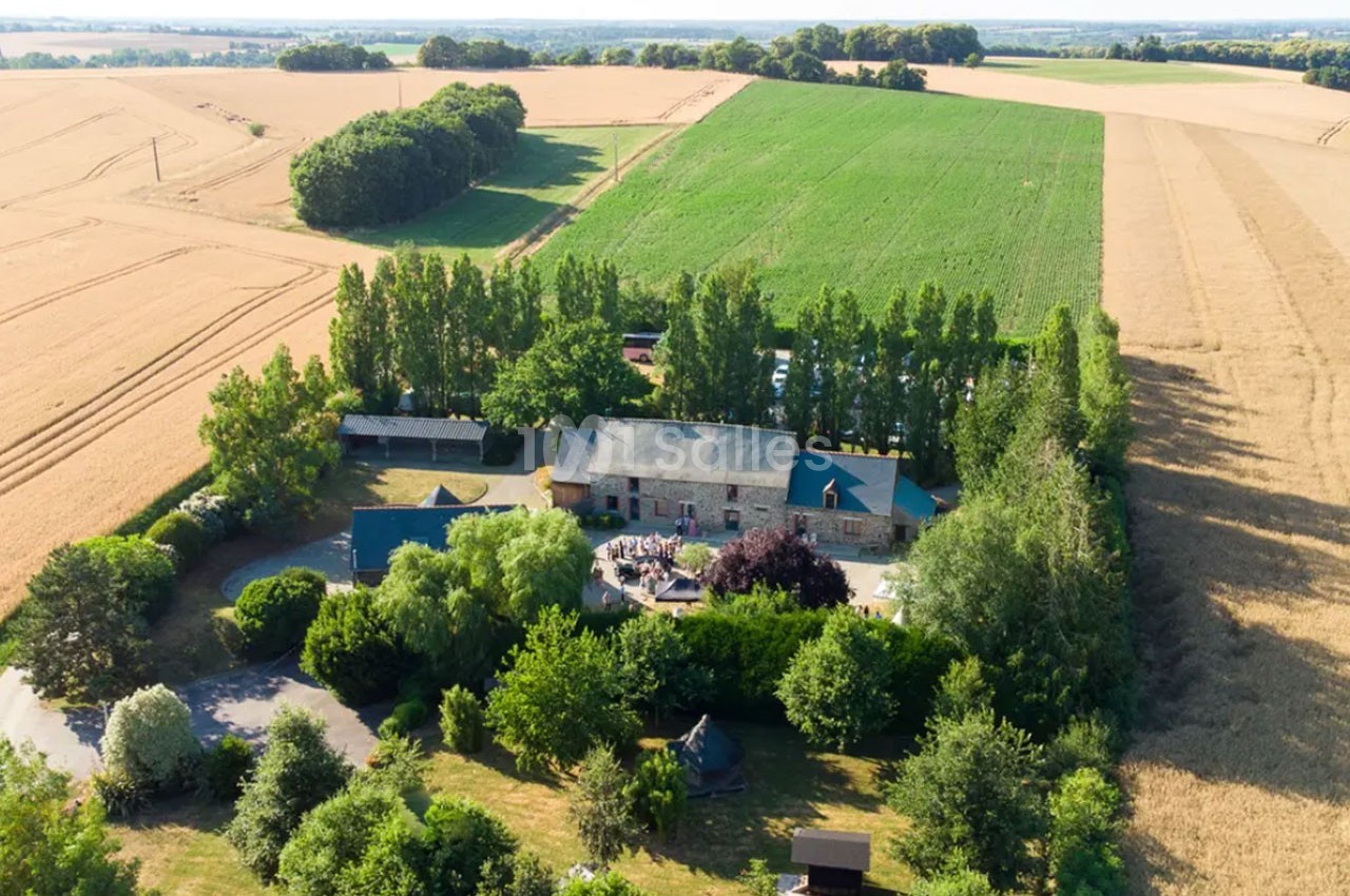 Vue aérienne d'une ferme entourée de champs cultivés, d'arbres et de verdure en pleine campagne.