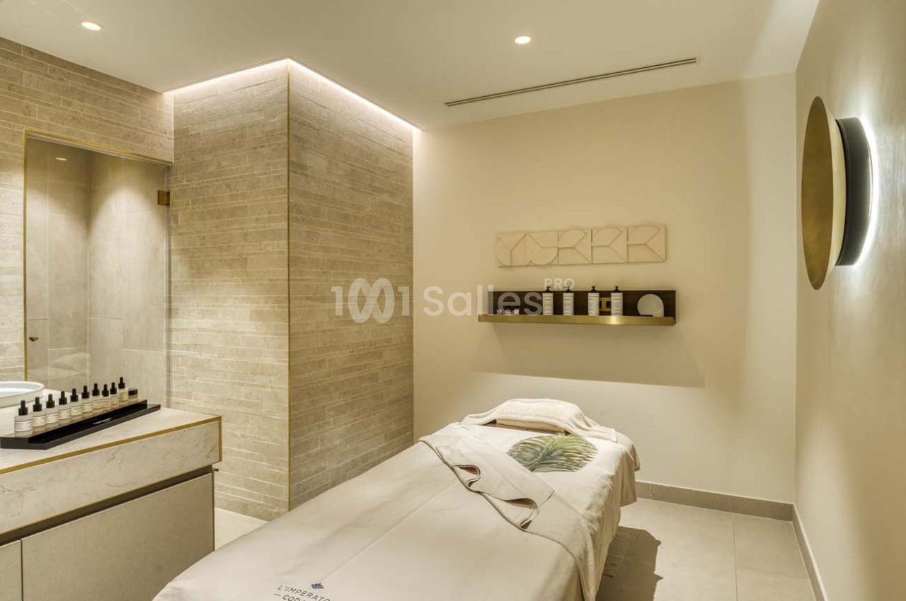 Salle de soins avec table de massage, éclairage doux, étagère avec produits et mur en briques claires.