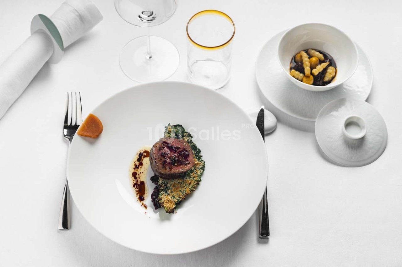 Assiette gastronomique avec viande, légumes verts, sauce au vinaigre balsamique et noix dans un bol à côté.