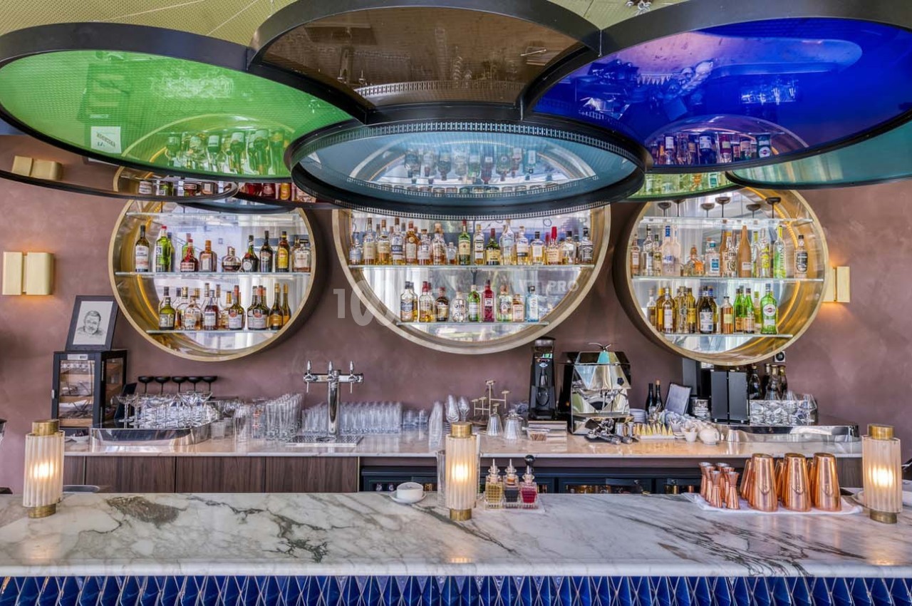Bar moderne avec comptoir en marbre, étagères circulaires illuminées contenant des bouteilles d'alcool et des verres.