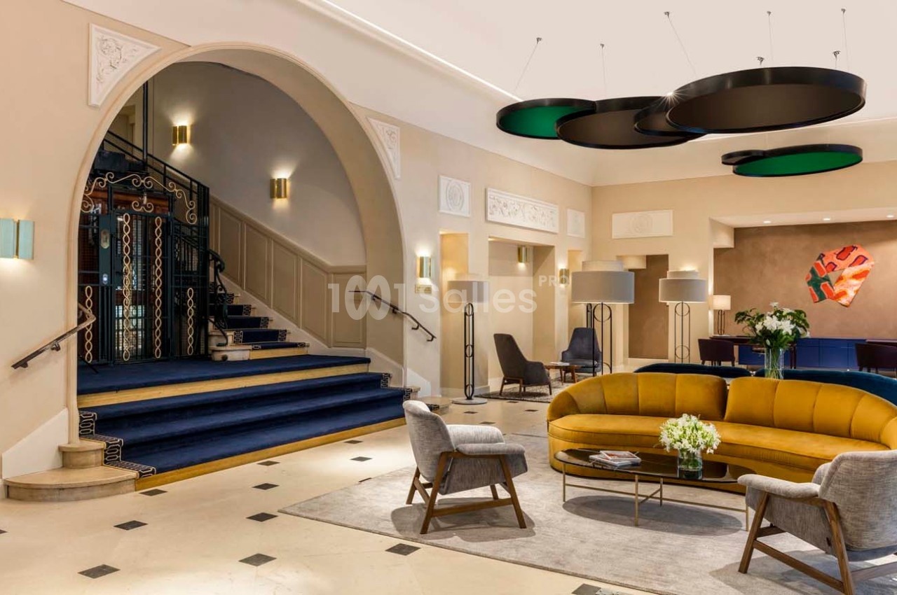 Hall d'entrée élégant avec escalier, canapé jaune, fauteuils et luminaires modernes dans un décor lumineux.