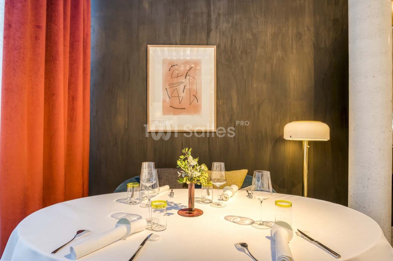 Table dressée avec élégance, décorée d'un bouquet, entourée de rideaux rouges et éclairée par une lampe moderne.