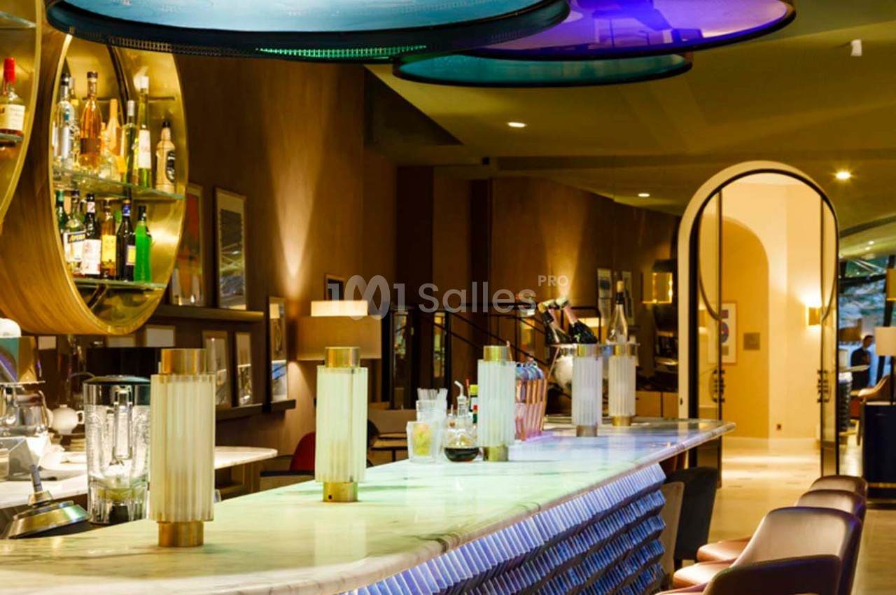Bar élégant avec comptoir en marbre, tabourets alignés, étagères de bouteilles et éclairage moderne coloré.