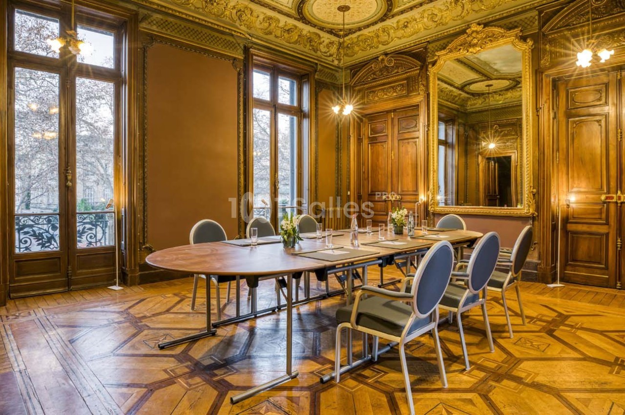 Salle de réunion élégante avec table ovale, chaises modernes, parquet en bois et miroirs ornés sur les murs.