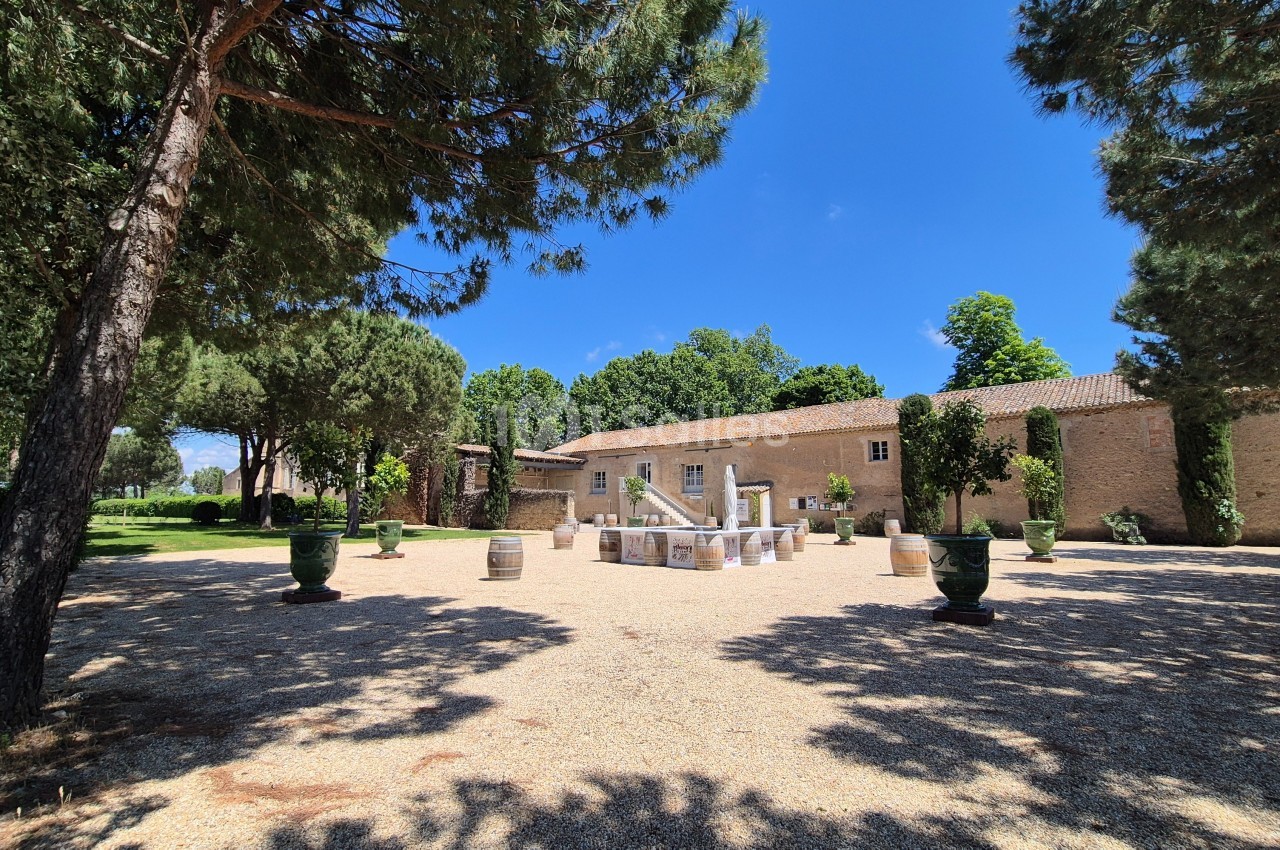 Cour ensoleillée avec fontaine centrale, entourée d'arbres, de pots décoratifs et d'un bâtiment en pierre.