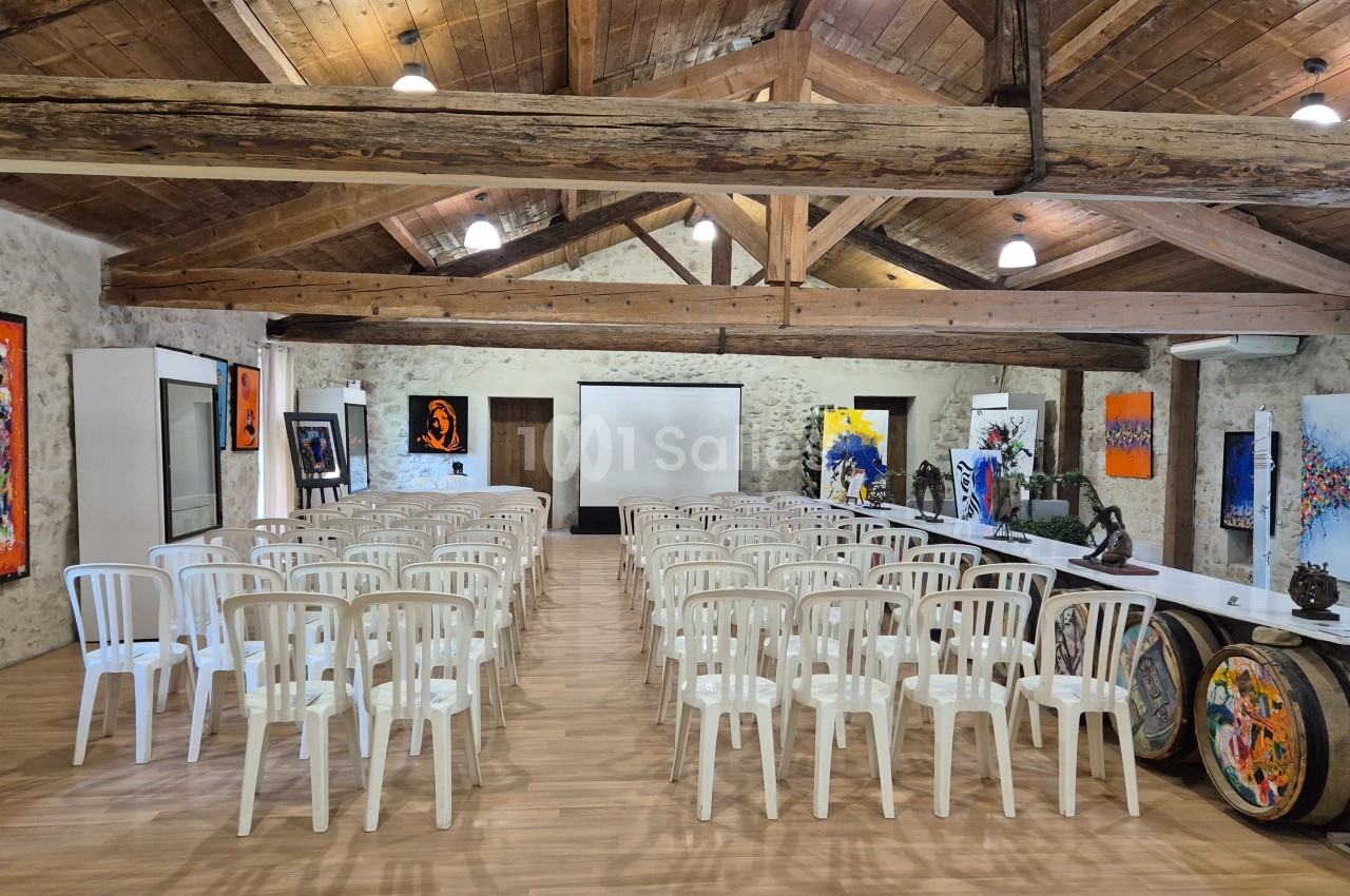 Salle de réunion avec des chaises blanches alignées, des œuvres d'art accrochées aux murs et un plafond en poutres…