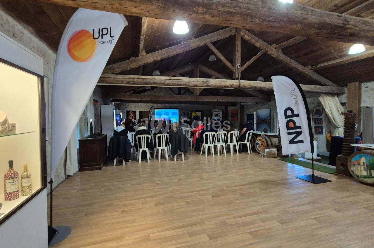 Salle avec des participants assis face à une présentation, entourée de drapeaux publicitaires et d'éléments décoratifs.