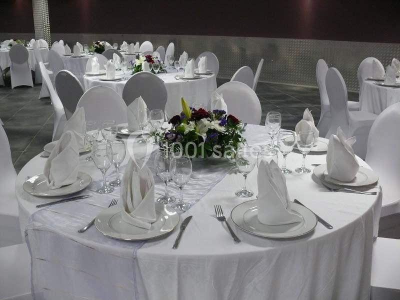 Tables rondes élégamment dressées avec nappes blanches, serviettes pliées, verres et centres de table fleuris.