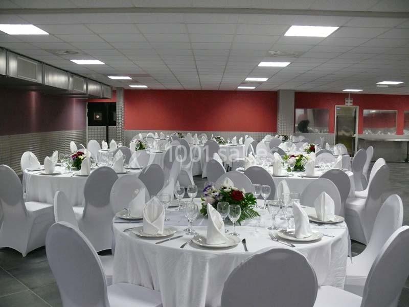 Salle de réception avec tables rondes dressées, nappes blanches, chaises couvertes et décorations florales.
