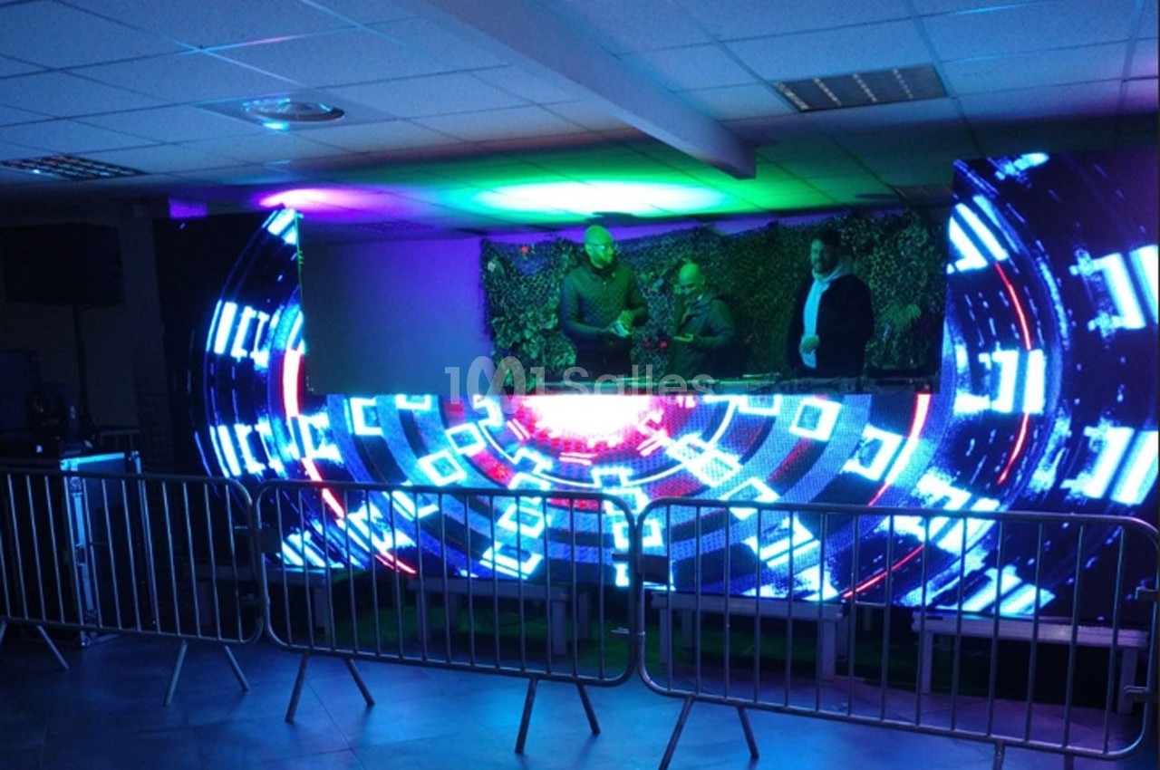 Trois DJ mixent sur une scène illuminée par un écran LED affichant des motifs lumineux futuristes.