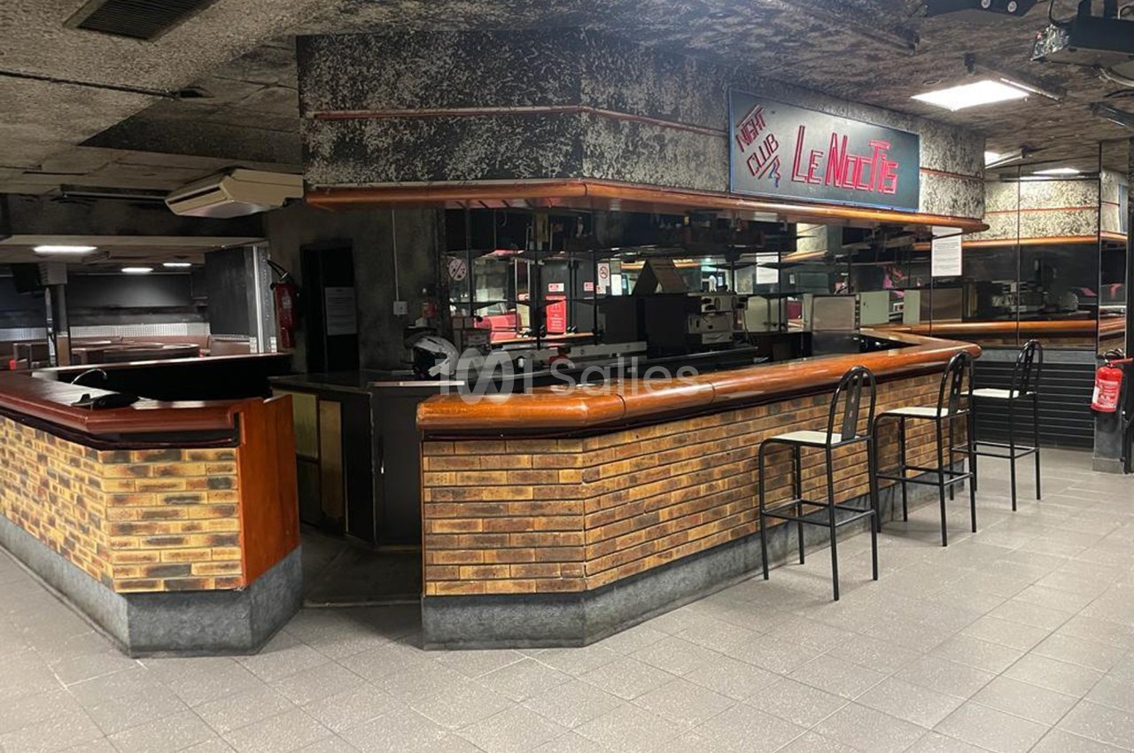 Comptoir d'un bar en briques avec tabourets, situé dans un espace intérieur au style rétro industriel.
