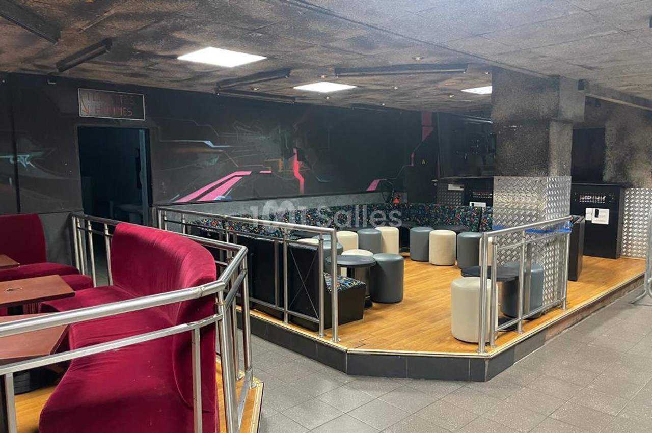 Espace intérieur avec banquettes colorées, tabourets et tables, éclairage artificiel et murs sombres décorés.