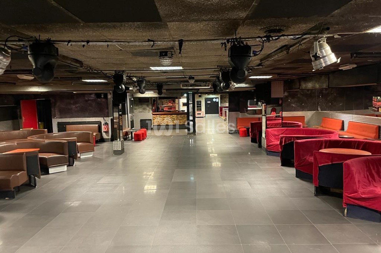 Salle vide avec banquettes rouges et marron, sol en carrelage gris, éclairage tamisé et plafond sombre.