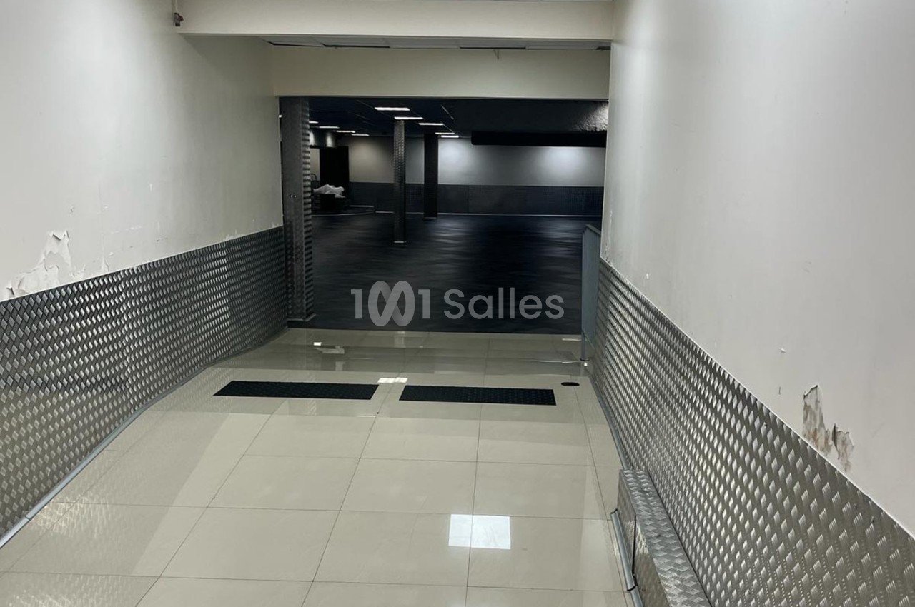 Rampe inclinée avec revêtement métallique menant à un espace intérieur sombre au sol noir et murs clairs.