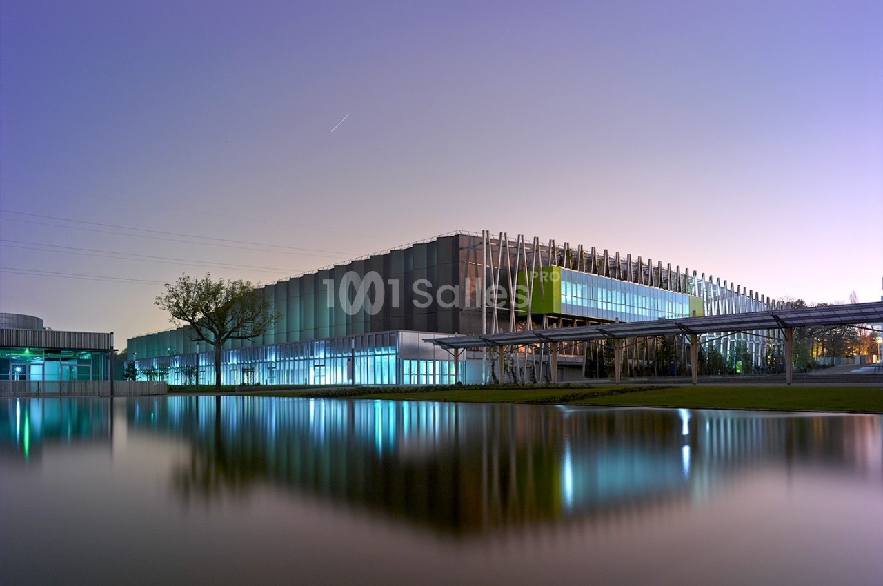 Bâtiment moderne avec façade vitrée, éclairé au crépuscule, reflété dans un plan d'eau calme.