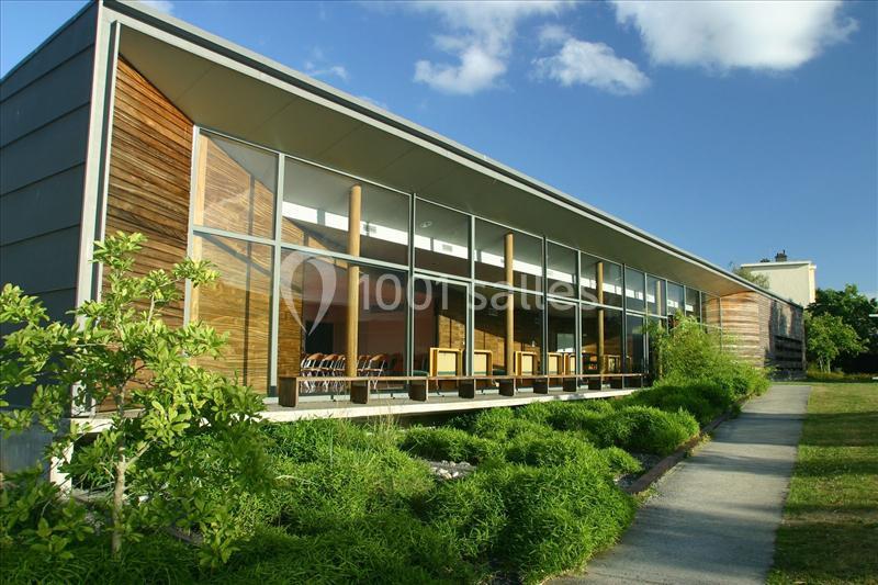Bâtiment moderne avec façade en verre et bois, entouré de verdure et éclairé par la lumière naturelle.