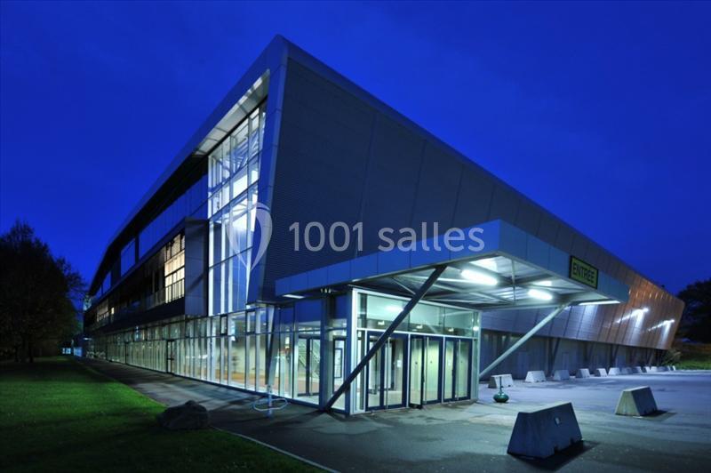 Bâtiment moderne éclairé de nuit avec une façade vitrée et une entrée principale visible au premier plan.