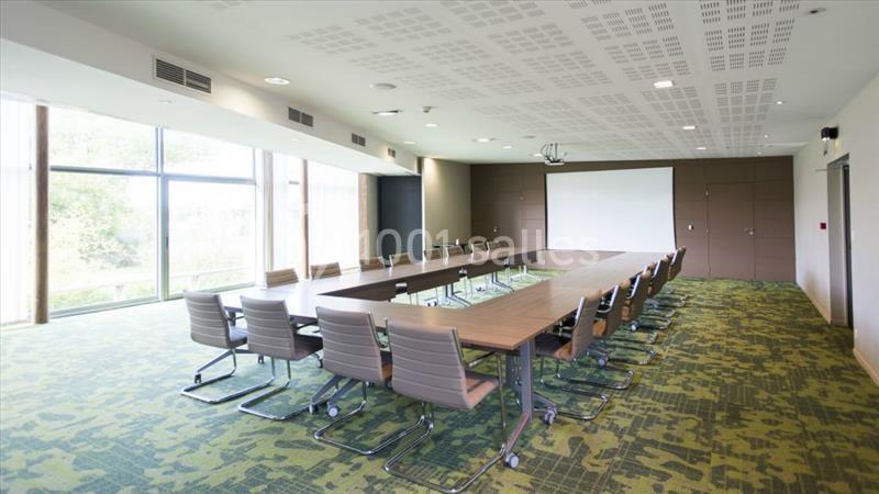 Salle de réunion lumineuse avec une grande table rectangulaire, des chaises modernes et un écran de projection.