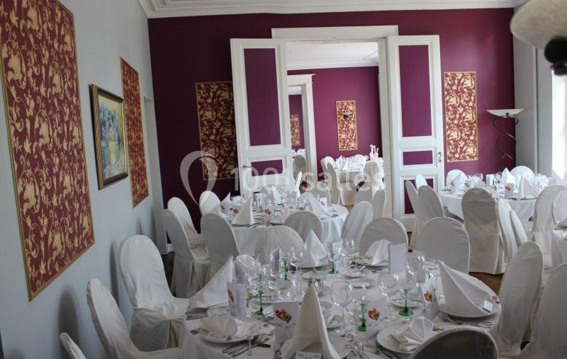 Salle de réception élégante avec tables dressées, nappes blanches et décorations murales rouges à motifs dorés.
