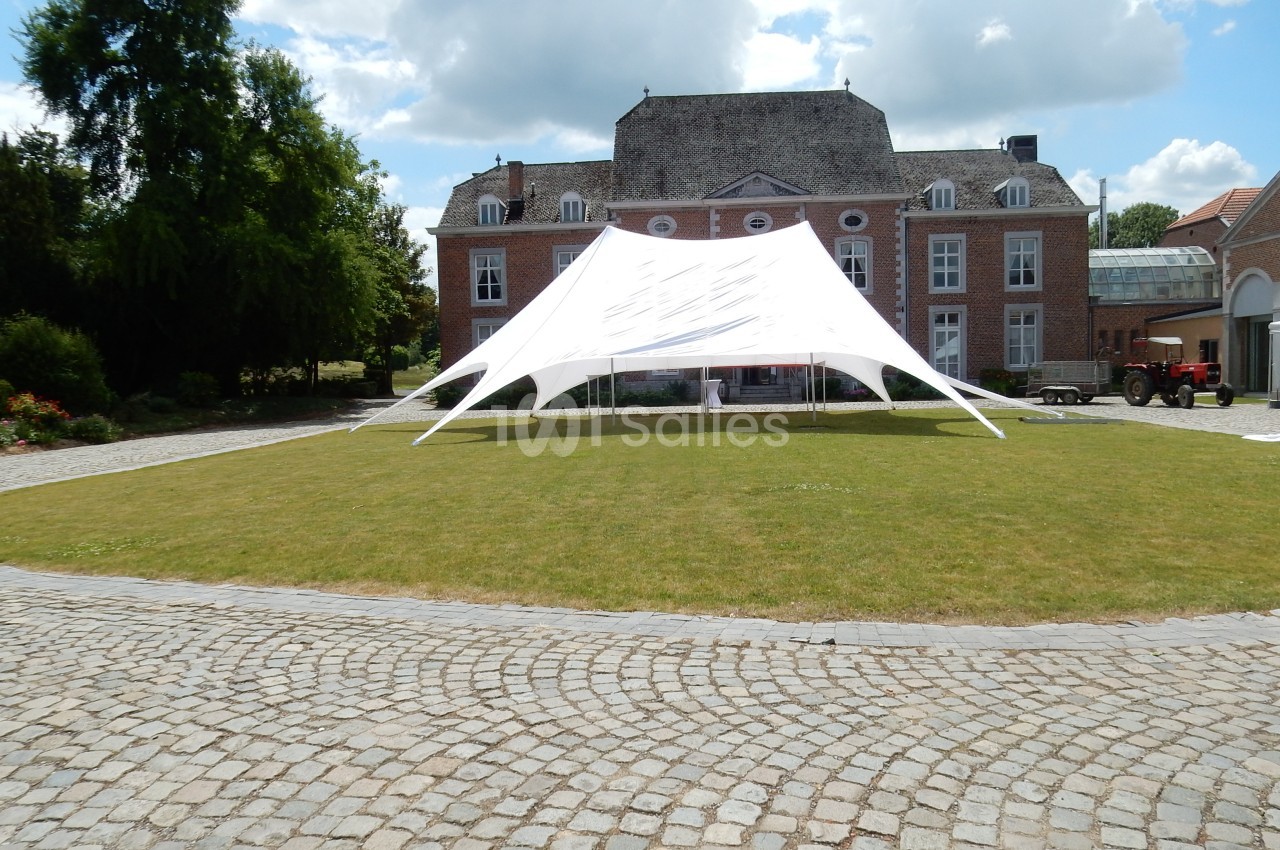 Tente blanche installée sur une pelouse devant un bâtiment en briques rouges avec des fenêtres à volets blancs.