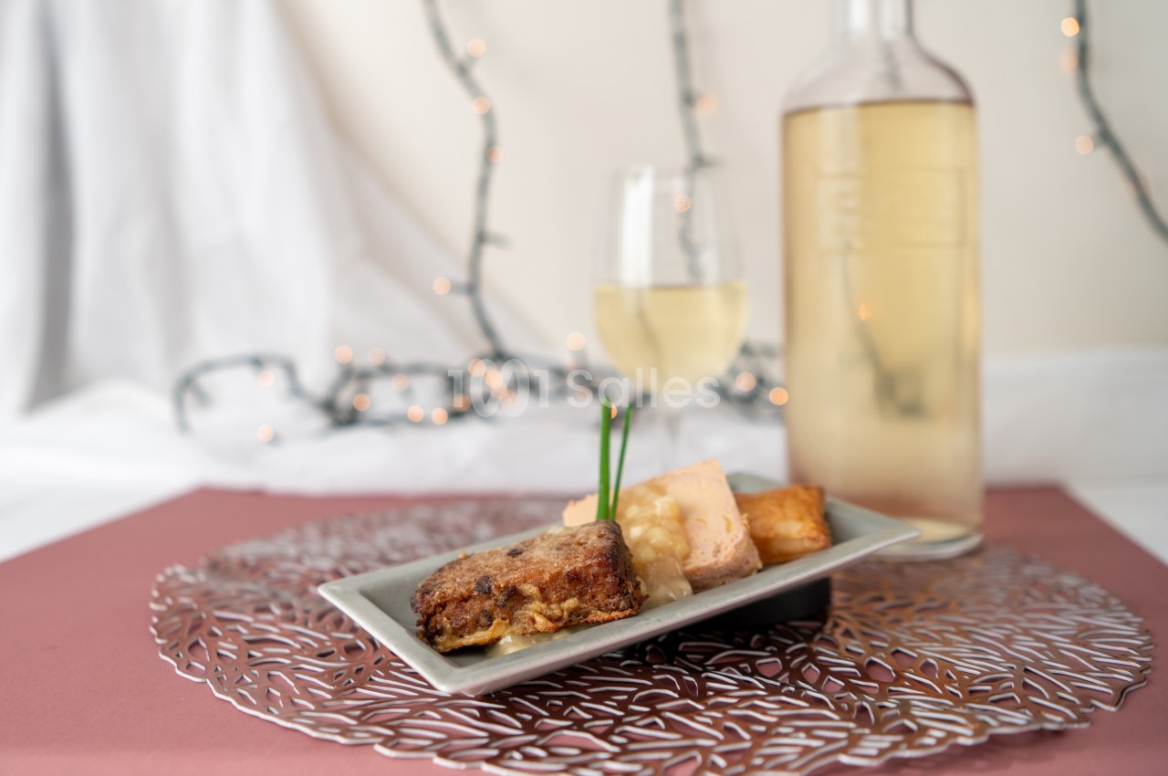 Assiette de dégustation avec foie gras, pain grillé et accompagnements, servie avec un verre et une bouteille de vin blanc.