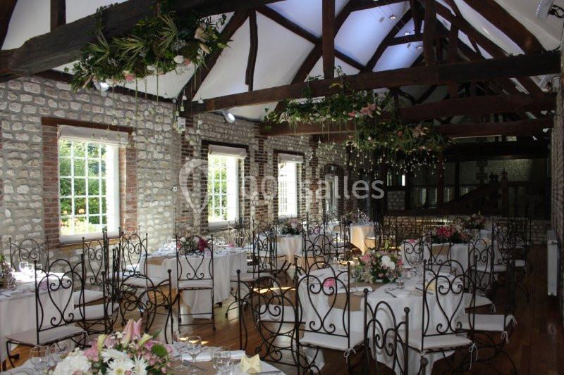 Salle de réception lumineuse avec murs en pierre, poutres apparentes et tables décorées de fleurs.