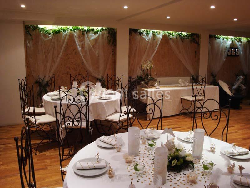 Salle décorée pour un événement, avec tables rondes dressées, chaises en fer forgé et ornements végétaux.