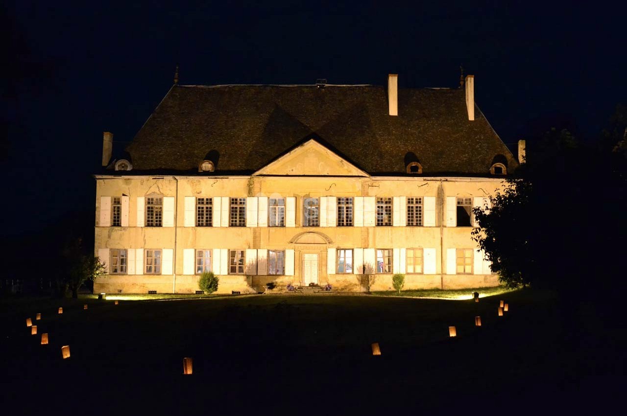 Façade d'un grand bâtiment ancien éclairé la nuit, entouré de petites lumières au sol.