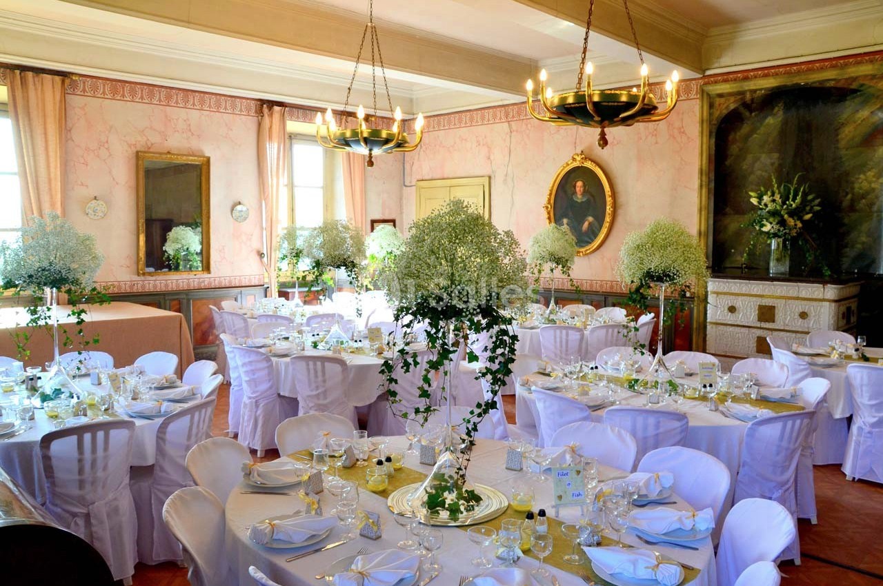 Salle de réception élégante avec tables rondes dressées, nappes blanches et décorations florales raffinées.