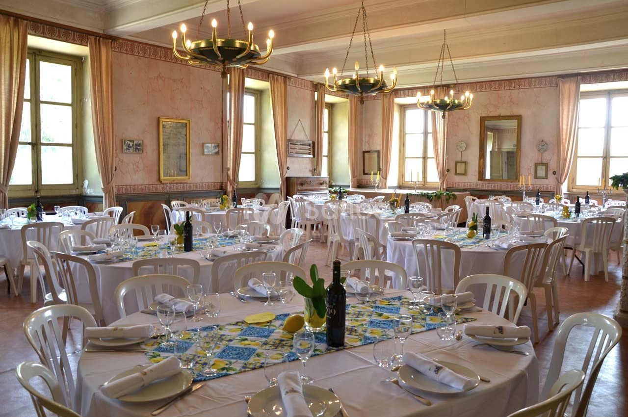 Salle de réception lumineuse avec tables rondes dressées, nappes blanches et décorations colorées.