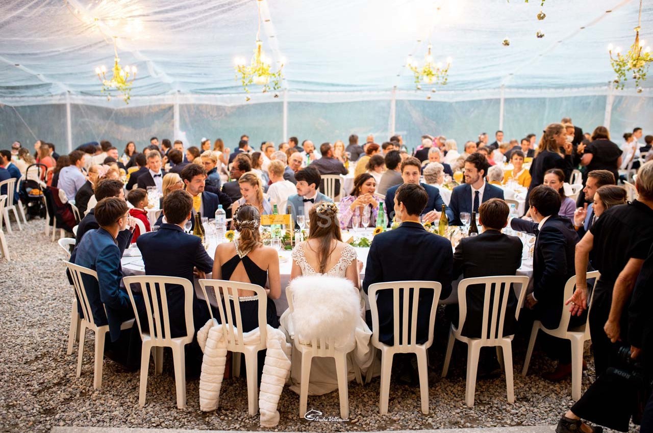 Des convives assis autour de tables sous une tente transparente lors d'un événement festif en plein air.