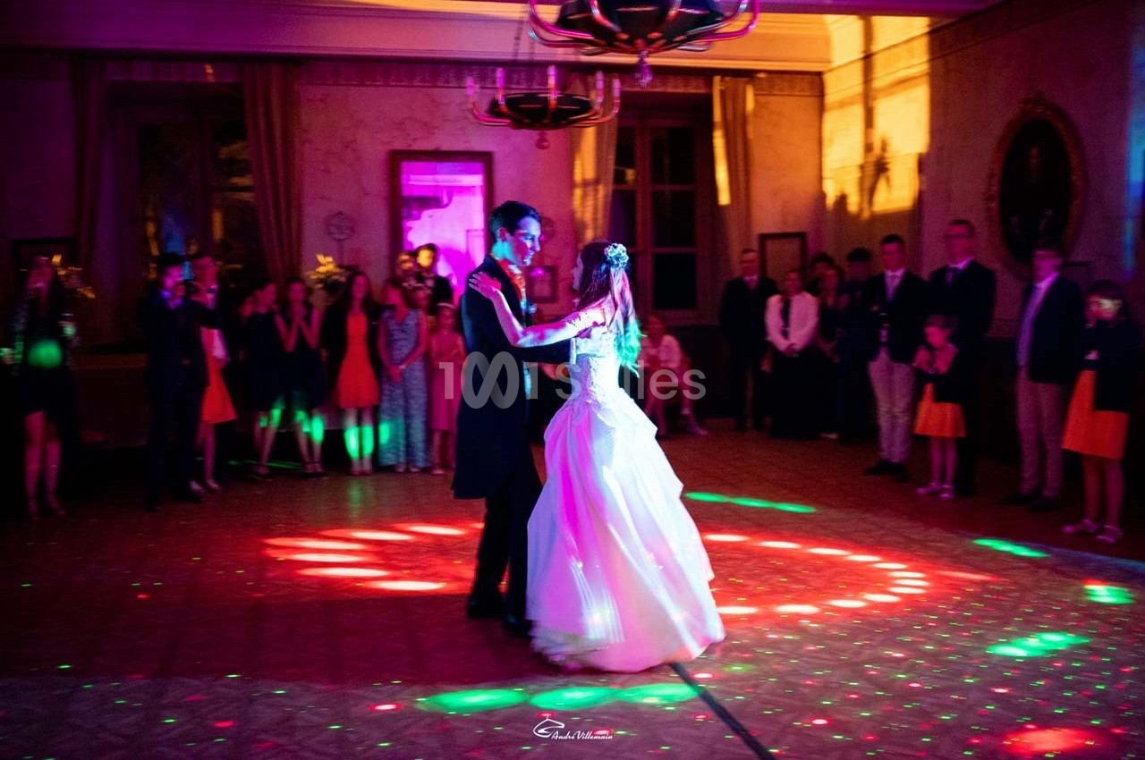 Un couple danse au centre d'une salle éclairée par des lumières colorées, entouré d'invités en tenue de soirée.