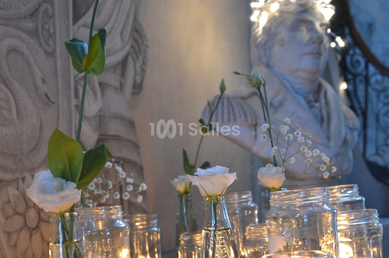 Bougies allumées et fleurs blanches dans des vases en verre devant une statue en arrière-plan.