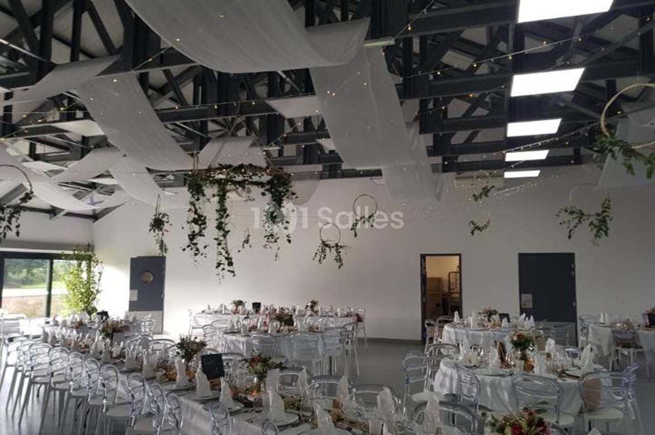 Salle de réception décorée avec des tables dressées, des voilages suspendus et des éléments végétaux.