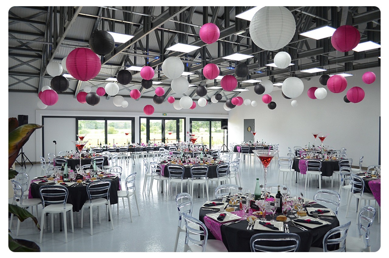 Salle de réception décorée avec des lanternes suspendues roses, blanches et noires, tables dressées pour un événement.