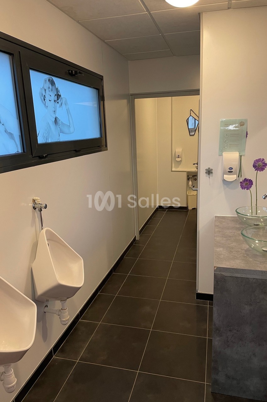 Salle de bain moderne avec urinoirs, lavabos en verre, distributeur de savon et décorations murales.