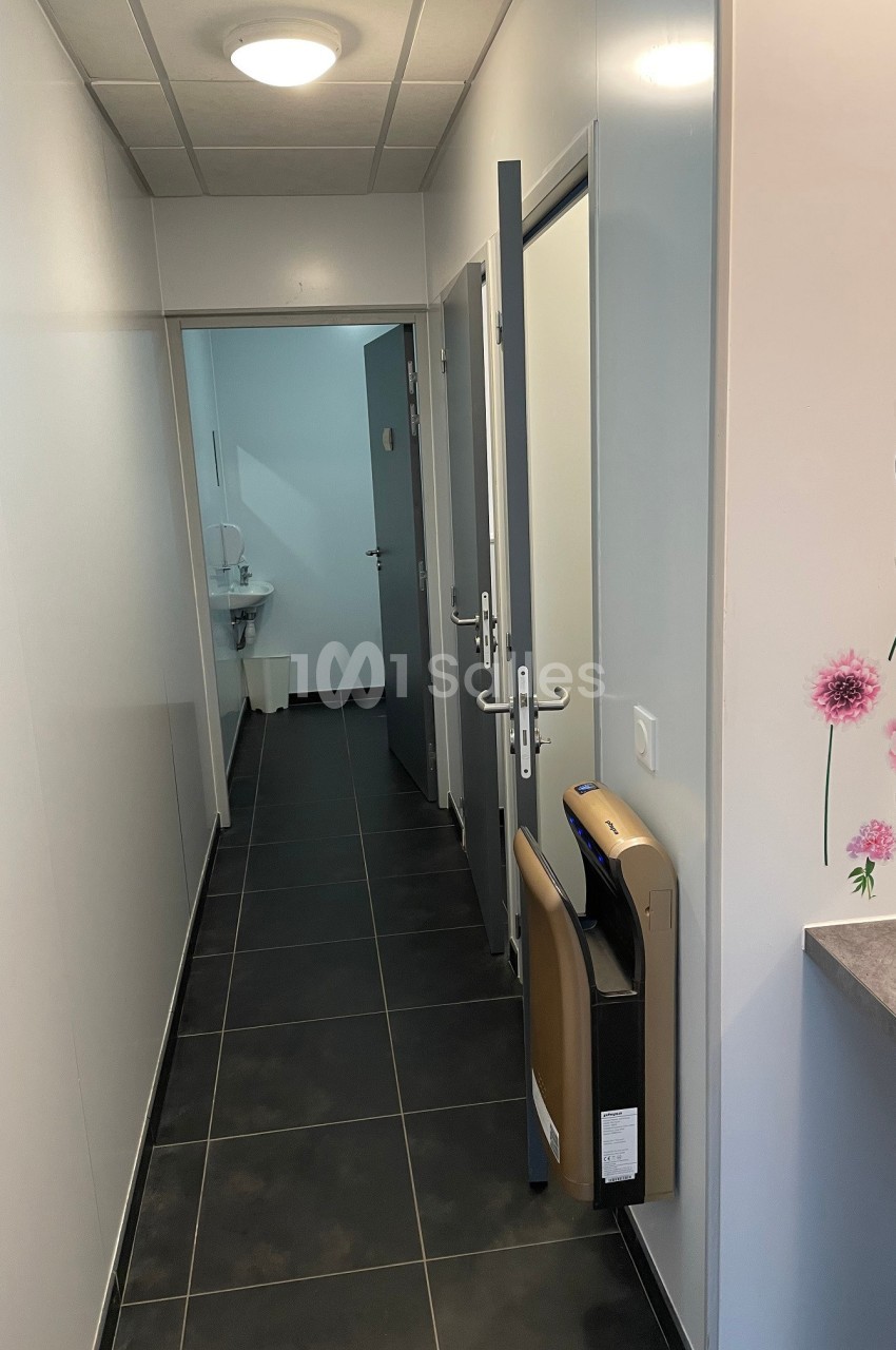 Couloir étroit avec sol en carrelage noir, portes ouvertes sur des pièces et décor floral sur un mur.