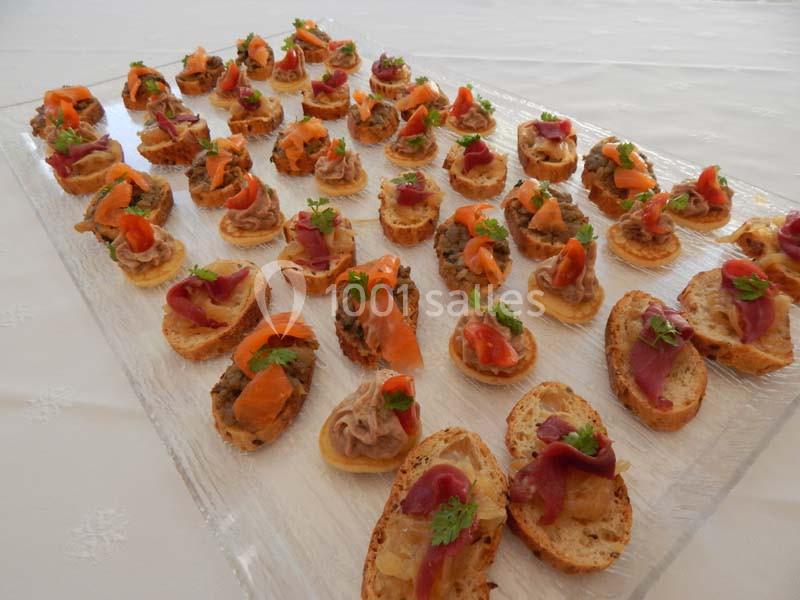 Plateau de canapés variés garnis de saumon, viande et herbes fraîches, disposés sur une nappe blanche.