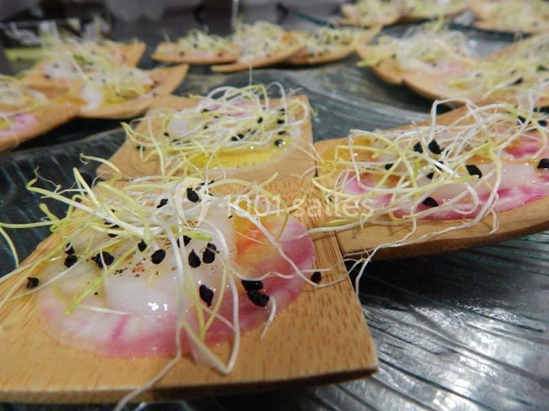 Tranches de carpaccio de poisson garnies de graines germées et de perles noires, présentées sur des supports en bois.