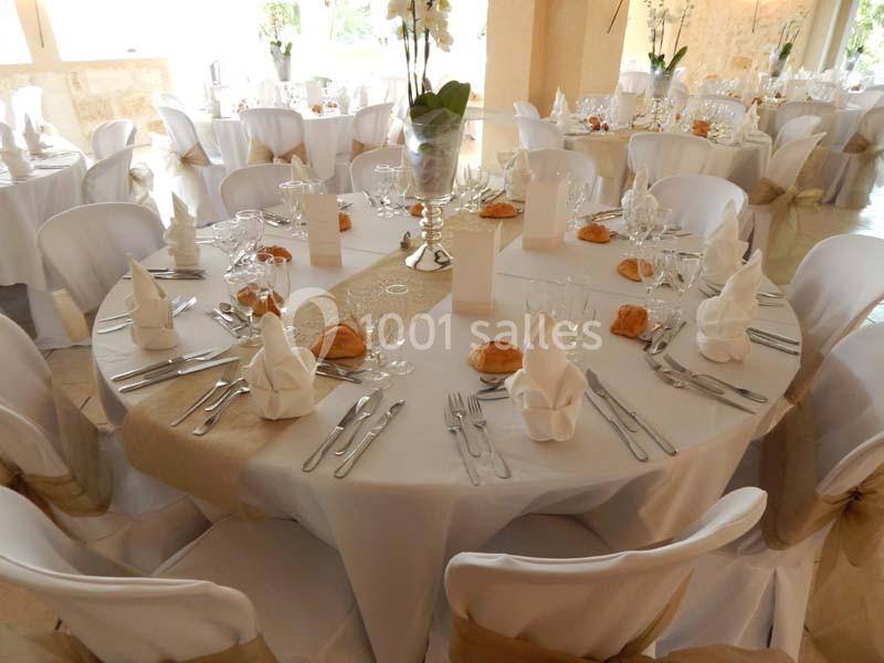 Tables rondes élégamment dressées avec nappes blanches, serviettes pliées, couverts, verres et petits pains.