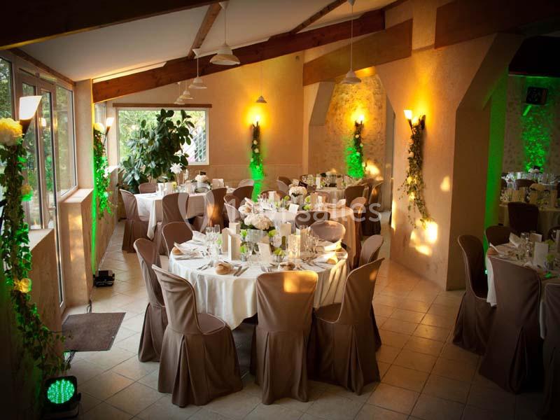 Salle de réception décorée avec des tables rondes, nappes blanches, chaises marron et éclairage chaleureux.