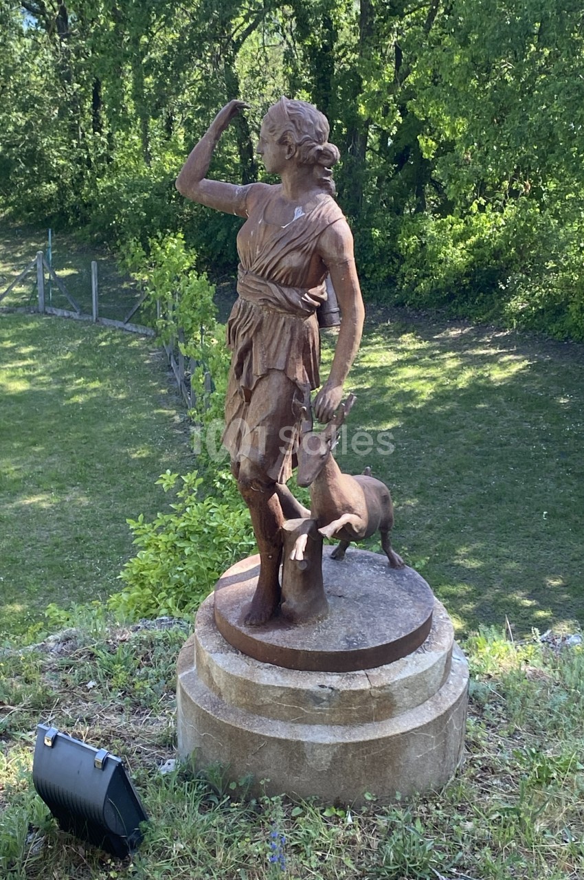 Statue en bronze représentant une femme debout avec un cerf, située dans un parc verdoyant.